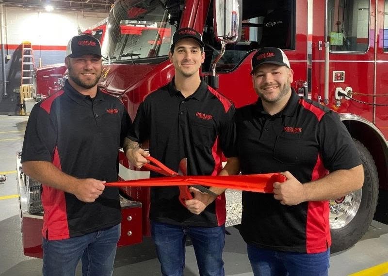 REDLINE Fire Watch New Jersey team performing a ribbon cutting at a New Jersey fire station, wearing branded REDLINE polos in front of a fire engine.
